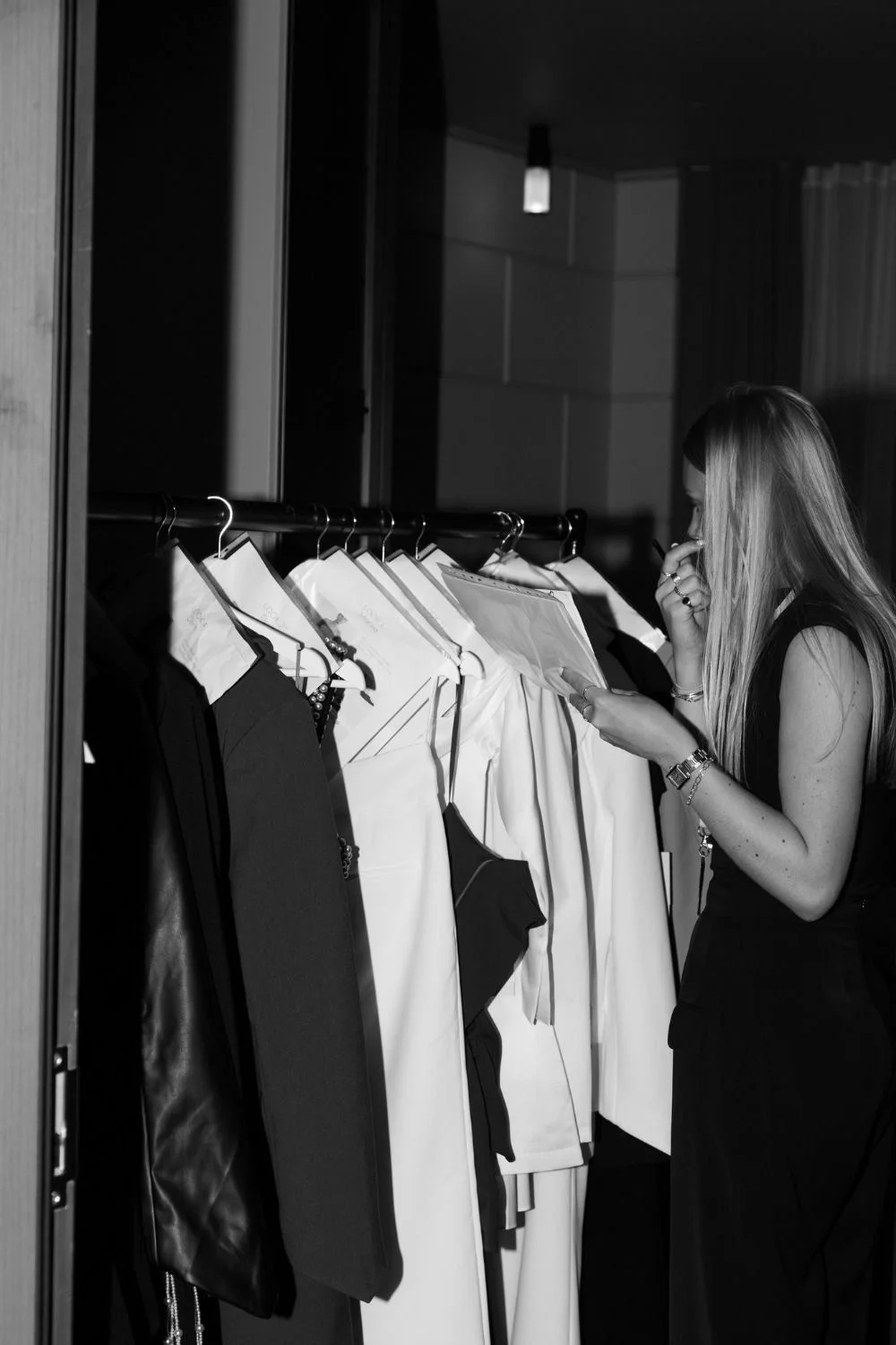 Woman reviewing garments and wardrobe notes beside a clothing rail