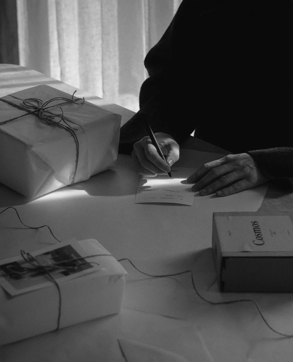 A person writing a personal note beside gifts wrapped in paper and twine