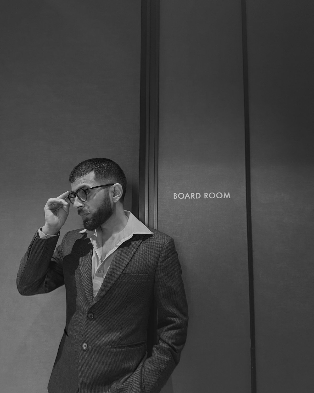 Man adjusting his glasses in a tailored suit beside a boardroom entrance
