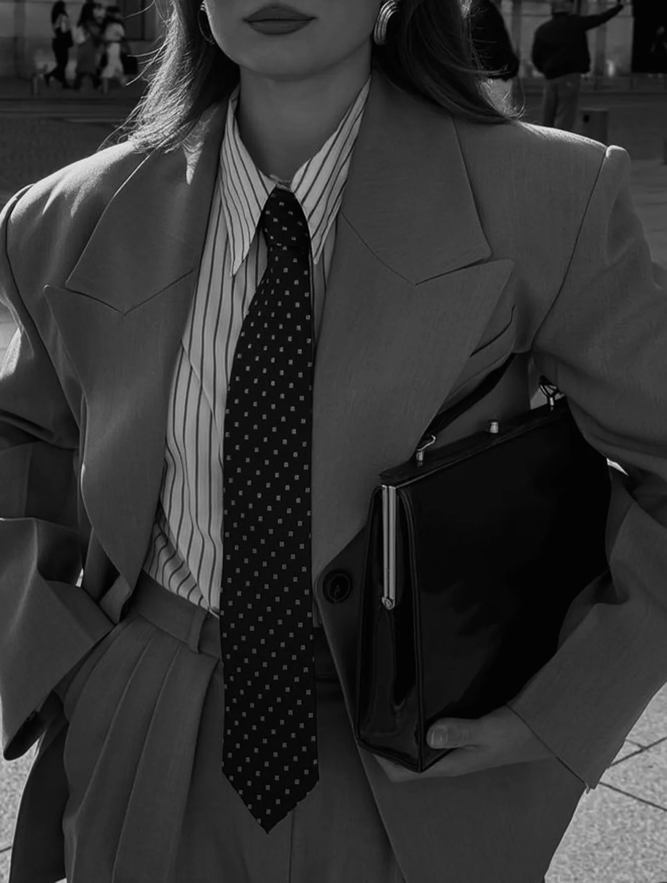 Woman wearing a tailored blazer, striped shirt and tie while carrying a black portfolio