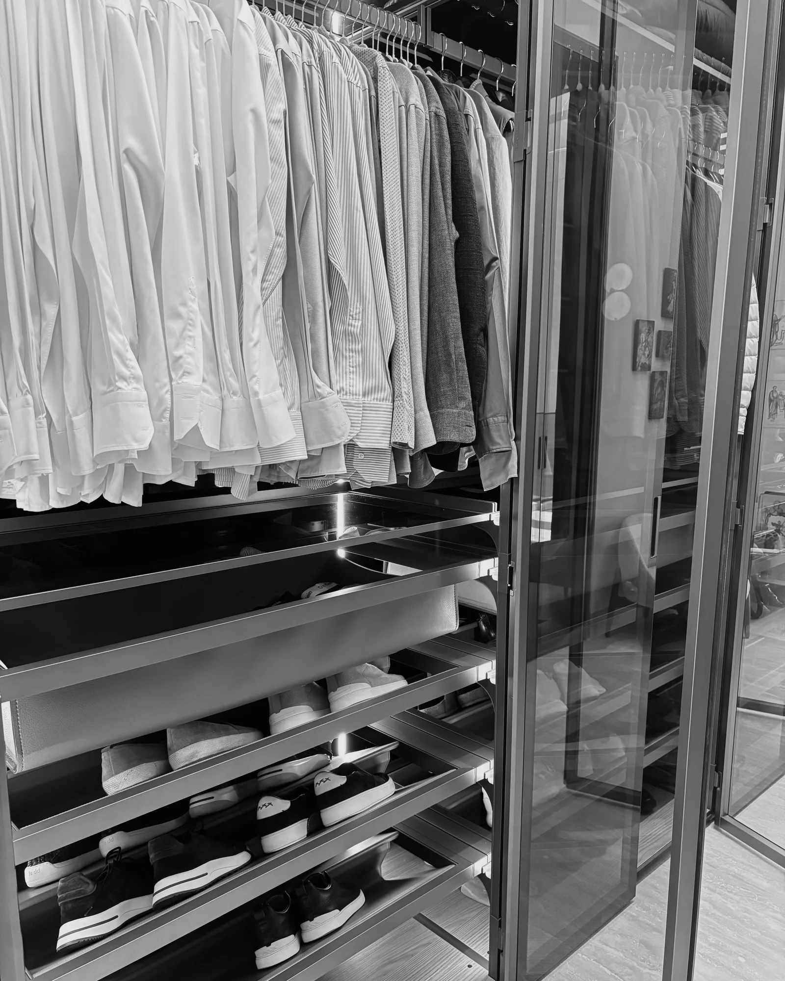 Tailored shirts, jackets and shoes arranged in a glass-fronted wardrobe