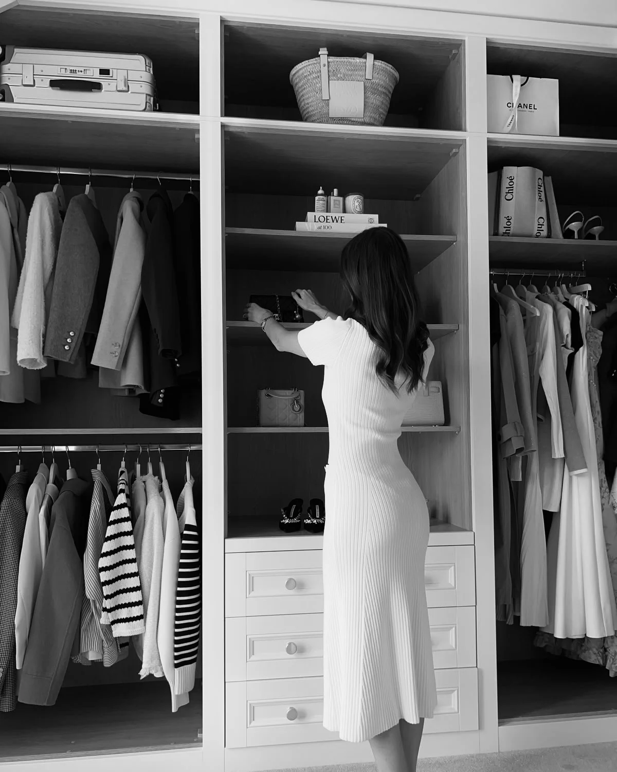 Woman arranging handbags in an organised wardrobe with clothing and accessories